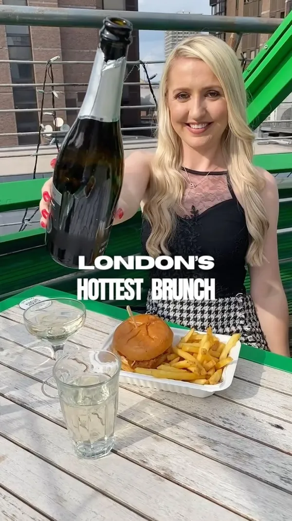 The video showcases Bar Elba's bottomless drag brunch.  The setting is a rooftop bar with vibrant yellow and green decor, string lights, and lush greenery. Food shown includes burgers and fries, presented in simple, disposable containers. Drinks featured are Prosecco and cocktails.  The video emphasizes the fun, lively atmosphere and the inclusion of drag performances. No specific dietary information is provided. The main focus is on the overall experience of the brunch, highlighting the food, drinks, entertainment, and venue ambiance.