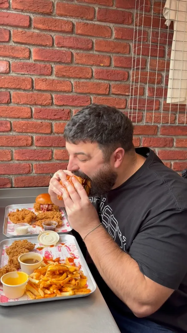 The video showcases Butchies Buttermilk Fried Chicken in London. It features the exterior of the restaurant, followed by a view of the menu board. The video then shows a man holding trays of food, including fried chicken sandwiches, chicken tenders, and fries. Close-up shots highlight the food's presentation, including sauces and toppings. The man is then seen assembling and eating the food. The video ends with a shot of the restaurant's exterior.