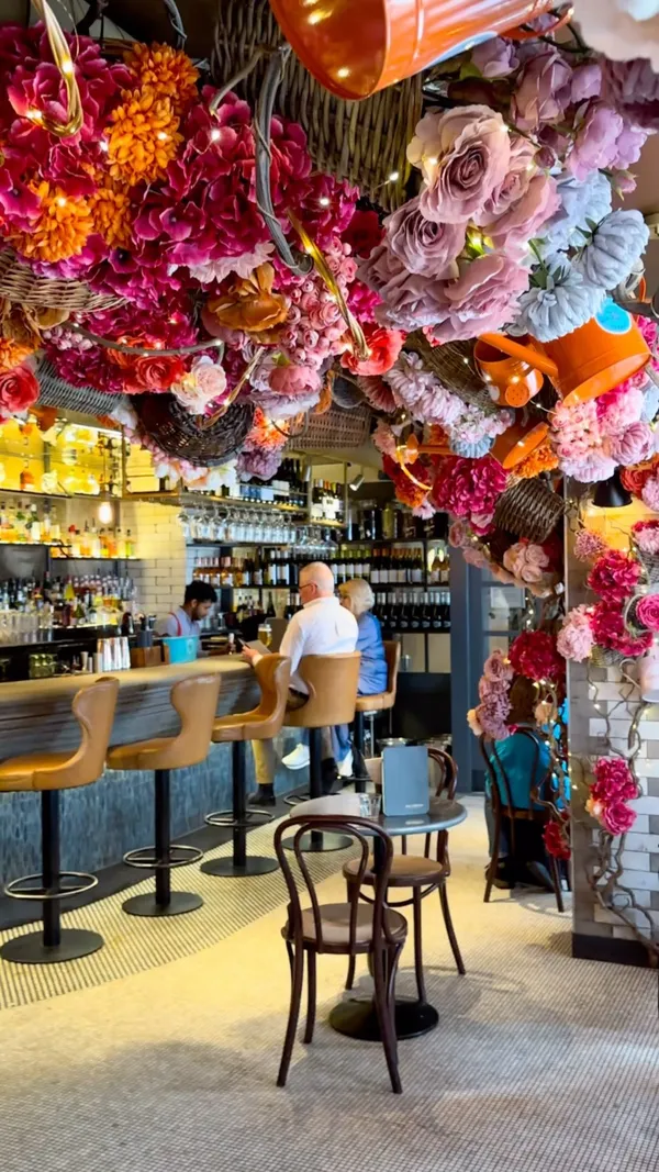 The video showcases Old Compton Brasserie in London. It features the restaurant's summer terrace, which is heavily decorated with flowers. The video highlights various food and drink items, including Aperol spritzes, coffee, and a banana split. It also shows the bar area and the restaurant's interior. The main focus is on the ambiance and aesthetics of the venue, with food and drinks serving as supplementary elements.