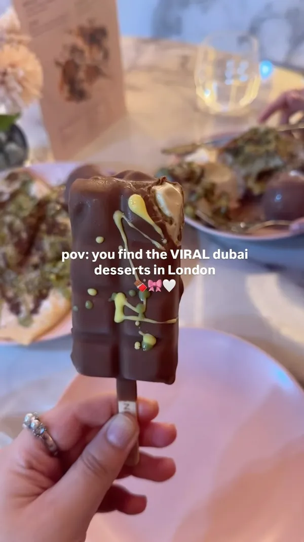 The video showcases Snowflake Gelato in London, highlighting their Dubai-inspired desserts, particularly pistachio kunafe variations. It features a crepe, a waffle, and a gelato stick, all drizzled with chocolate and pistachio toppings, served on pink plates. The presentation emphasizes the desserts' textures and rich toppings. No specific dietary information is mentioned. The main focus is a showcase of the desserts.