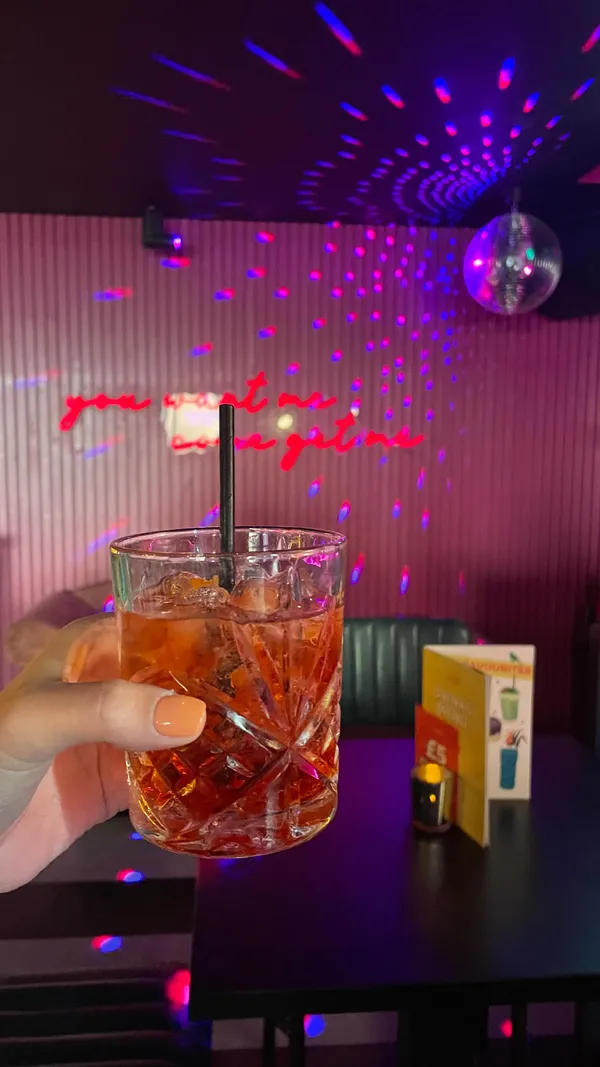 The video showcases the preparation and enjoyment of Negroni Sbagliato cocktails in a vibrant, dimly lit bar setting.  The cocktails are presented in short rocks glasses with ice and an orange peel garnish. The bartender expertly mixes the drinks, emphasizing the inclusion of Prosecco. The video focuses on the preparation and the celebratory atmosphere surrounding the cocktails, with minimal emphasis on any food items.  No specific dietary information is mentioned.