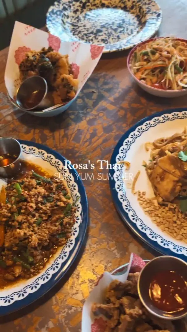 The video promotes the "Sun Yum Summer" menu at Rosa's Thai restaurant. It features a montage of various Thai dishes, including Pad Thai, a minced meat dish with rice and a fried egg (likely Pad Krapow), a papaya salad (Som Tum), fried appetizers like crispy beef/pork and tempura-style vegetables, and prawn crackers with dipping sauces. The video also shows the restaurant's interior, exterior signage, and people enjoying their meal, including a cheers with wine and beer. The overall theme is bright, summery, and appetizing.