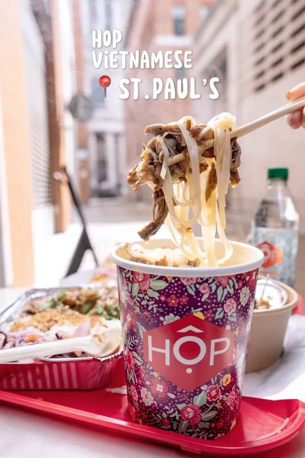The video showcases a variety of Vietnamese street food dishes from HOP Vietnamese in London, near St. Paul's Cathedral.  The food items include Pho, a Satay Chicken HOP Box meal, Caramel Chicken Noodle Salad, Shrimp Gyoza, and Chicken Strips. The presentation highlights the colorful and appetizing nature of the food, with various close-ups and shots of the food being eaten. Dietary information is not explicitly provided, although vegetarian options may be available based on the menu shown in a short screen recording. The primary focus is on showcasing the food and the convenience of ordering using a digital kiosk.