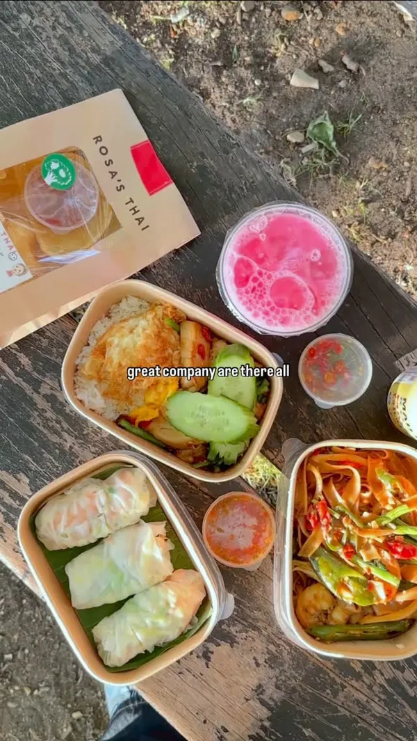 The video starts with the creator talking about living for everyday moments. It then shows the creator and a partner walking, picking up a takeaway order from Rosa's Thai restaurant, and heading to a park by the river for a picnic. The video showcases the takeaway bags, the food items (bubble tea, prawn rolls, a rice dish with fried egg and vegetables, and a noodle dish), and the couple enjoying their meal by the water.