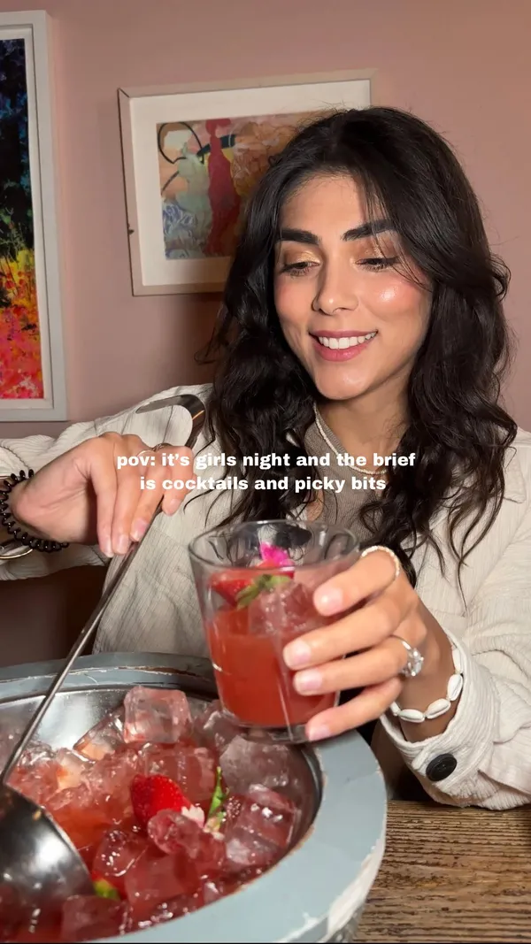 The video showcases a girls' night out at The Little Scarlet Door, a cocktail bar in London.  It features various cocktails, particularly a strawberry-based drink served in a large disco-ball-shaped container, along with a selection of bar snacks including dips with bread, olives, cured meats, and gherkins. The presentation focuses on vibrant colors and visually appealing arrangements of food and drinks.