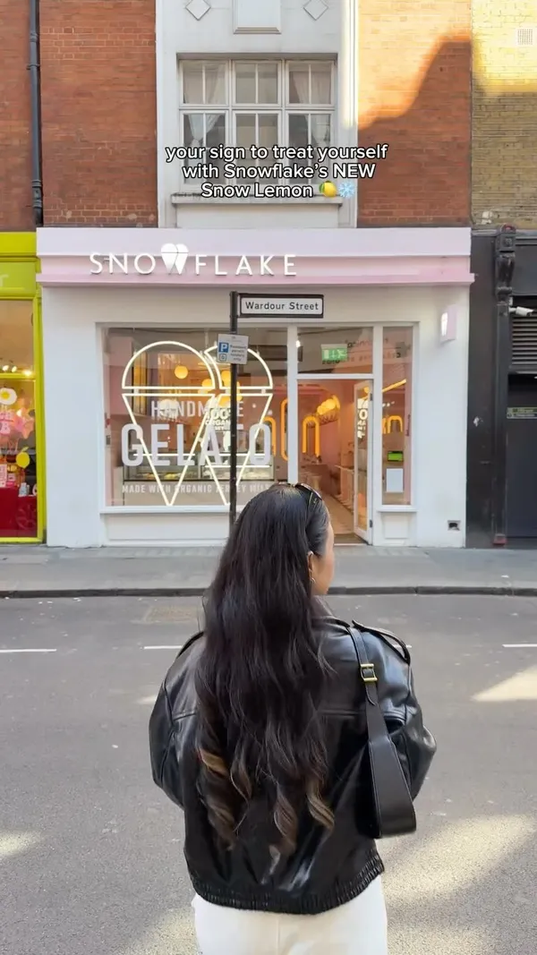 The video features a person walking towards a Snowflake Gelato shop. It shows close-ups of various gelato items in a display case, including mango and lemon shaped gelato. The scene shifts to a table setting with two lemon-shaped gelato popsicles, a pistachio milk cake, and an iced coffee. The person is shown picking up and biting into the lemon gelato popsicle and stirring the iced coffee.