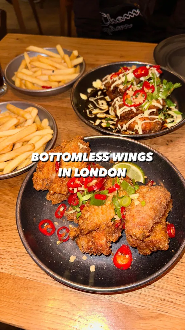 The video showcases a bottomless brunch at Wingmans Chicken in London. It features various types of chicken wings (Szechuan, Shanghai Oriental, and Sweet and Smokey BBQ), fries, and drinks. The food is presented on dark plates against a wooden table, highlighting the color and texture of the wings.  The video emphasizes the abundance of food, showing multiple plates of wings and fries. No specific dietary information is provided.