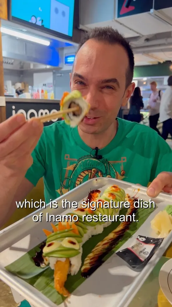 The video showcases Inamo restaurant in London’s Market Halls on Oxford Street. The content focuses on a meal featuring a Dragon Roll (sushi), a karaage chicken burger with fries, and Bang Bang Cauliflower.  The Dragon Roll is presented as a long sushi roll shaped like a dragon, garnished with avocado and sauces. The burger is topped with an Asian-style sauce, and the cauliflower is served in a spicy sauce. The video includes an Asian strawberry and lychee juice.  No specific dietary information is provided.
