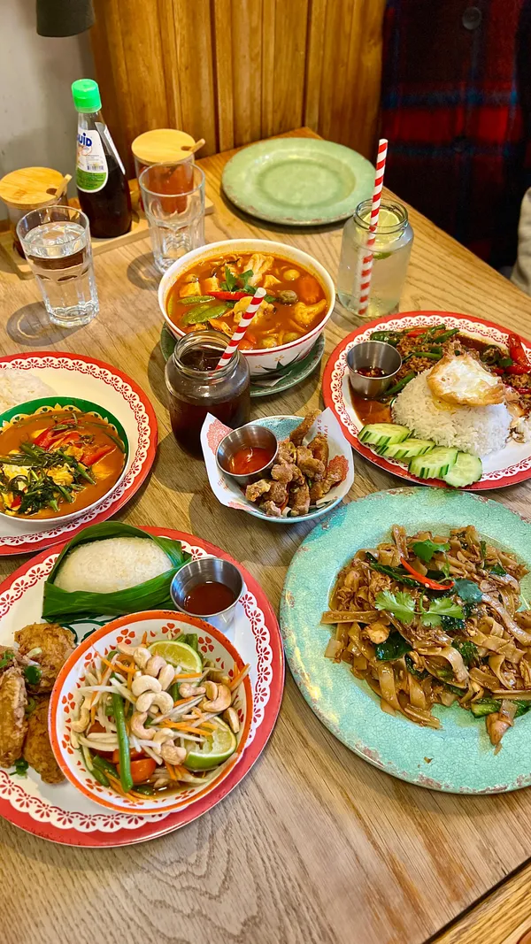 The video showcases a variety of Thai dishes from Rosa's Thai restaurant. It features dishes like stir-fried flat noodles, minced chicken stir fry with rice and fried egg, red curry with rice, Tom Yum soup, crispy pork bites, and papaya salad. The food is presented attractively on colorful plates. Dietary information is not explicitly provided, but the menu is shown and available on the website.