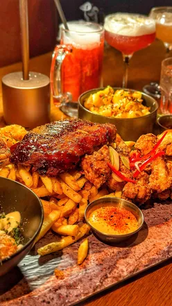 Ultimate Sharing Platter at The Alchemist UK with BBQ ribs, fried chicken, macaroni cheese, truffle tater tots, and cocktails.