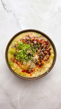 Bowl of instant noodles with spring onions, Parmesan, pancetta, egg yolk, sesame seeds, and chili oil, capturing a cozy ramen vibe.