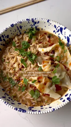 Spicy peanut noodles with gyozas, garnished with coriander and chili oil, perfect quick meal for hangovers.