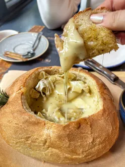 Whole Camembert cheese baked in a bread loaf with melted cheese pull, perfect for cheese lovers.