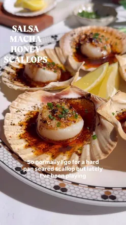 Salsa macha and honey butter scallops on oven-safe shells, garnished with chives and lemon zest, served with crusty bread.