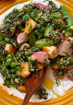 Hot halloumi salad with tahini Greek yogurt, radishes, peas, and herbs in a dreamy alfresco lunch setting.